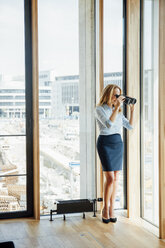 Geschäftsfrau mit Fernglas schaut aus dem Fenster - CHAF001778