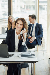 Smiling businesswoman at office desk on the phone - CHAF001787