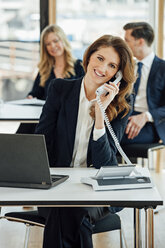 Smiling businesswoman at office desk on the phone - CHAF001788