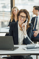 Smiling businesswoman at office desk on the phone - CHAF001789