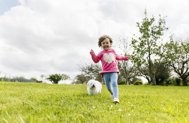 Smiling little girl running on a meadow with her dog - MGOF001923