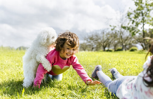 Zwei kleine Schwestern spielen mit ihrem Hund auf einer Wiese - MGOF001924