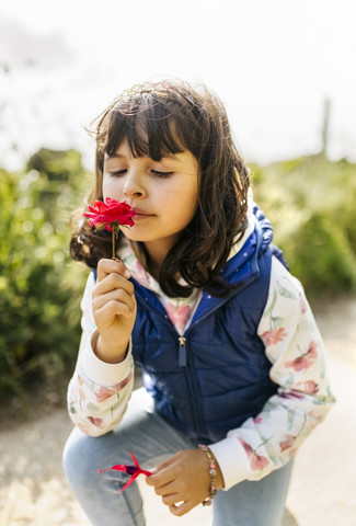Porträt eines kleinen Mädchens, das an einer roten Blume riecht, lizenzfreies Stockfoto