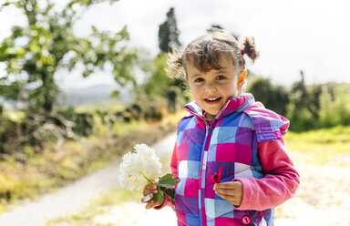 Porträt eines lächelnden kleinen Mädchens mit Blume in der Hand - MGOF001929