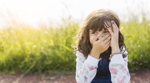 Portrait of little girl covering mouth with her hand while watching something stock photo