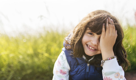 Porträt eines lächelnden kleinen Mädchens, das sein Auge mit der Hand bedeckt, lizenzfreies Stockfoto