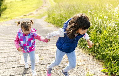 Two little sisters walking hand in hand on a path - MGOF001937