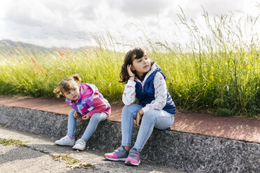 Two little sisters sitting on curb looking at distance - MGOF001939