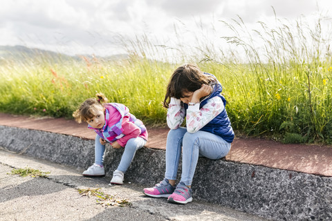 Two little sisters sitting at roadside waiting stock photo