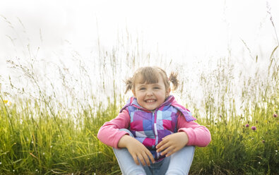 Happy little girl sitting in front of a meadow - MGOF001945