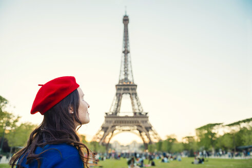 Frankreich, Paris, Champ de Mars, Frau mit roter Baskenmütze vor dem Eiffelturm mit Blick nach oben - GEMF000920