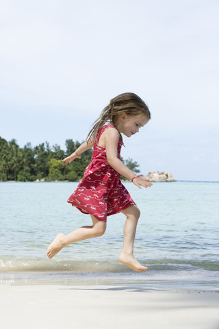 Thailand, girl in red dress jumping on beach stock photo