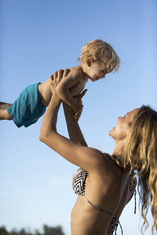 Glückliche Mutter im Bikini hebt ihren Sohn hoch, lizenzfreies Stockfoto