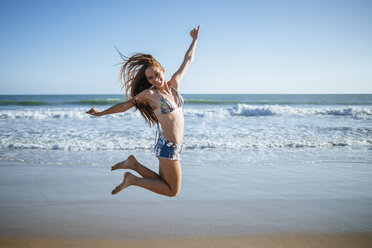 Enthusiastic young woman jumping on beach - KIJF000418