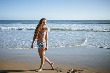 Smiling young woman walking on the beach - KIJF000420