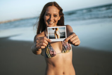 Happy young woman showing an instant photo on the beach - KIJF000429