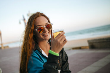 Young woman drinking beer by the sea - KIJF000433
