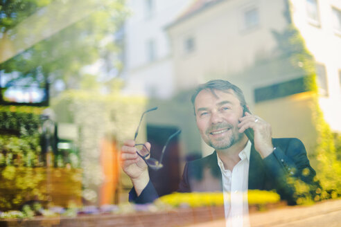 Geschäftsmann in einem Café hinter einer Fensterscheibe - MAEF011817