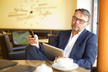 Porträt eines Geschäftsmannes mit digitalem Tablet und Smartphone, der in einem Café sitzt - MAEF011821