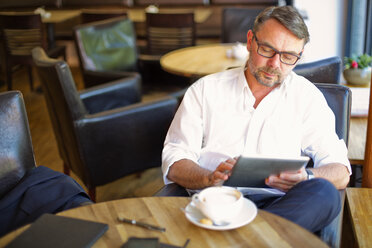 Businessman sitting in a coffee shop using digital tablet - MAEF011827