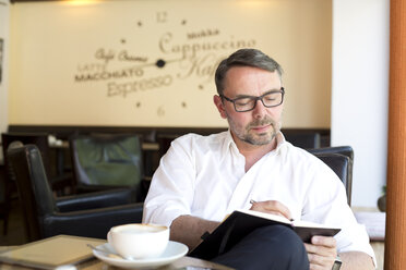 Porträt eines Geschäftsmannes, der in einem Café mit einem Notizbuch sitzt und etwas aufschreibt - MAEF011829