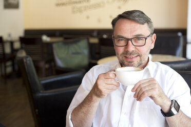 Porträt eines lächelnden Geschäftsmannes, der in einem Café sitzt und Kaffee trinkt - MAEF011831