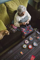 Häkelnde ältere Frau sitzt auf der Couch neben ihrer schlafenden Katze - RAEF001204