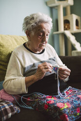Porträt einer häkelnden älteren Frau, die zu Hause auf der Couch sitzt - RAEF001207
