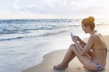Dominikanische Republik, Junge Frau am tropischen Strand, die ein mobiles Gerät benutzt - HSIF000458