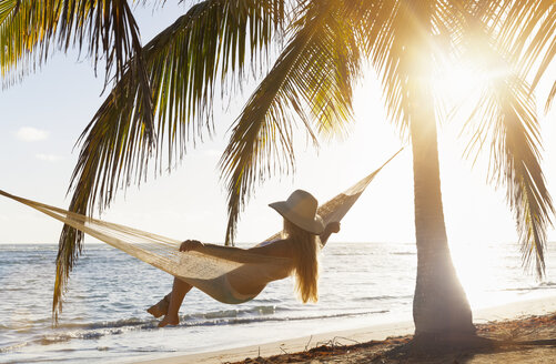 Dominican Rebublic, Young woman in hammock looking out over tropical beach - HSIF000461