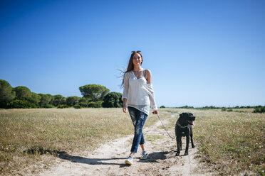 Junge Frau geht mit ihrem Hund in ländlicher Landschaft spazieren - KIJF000466