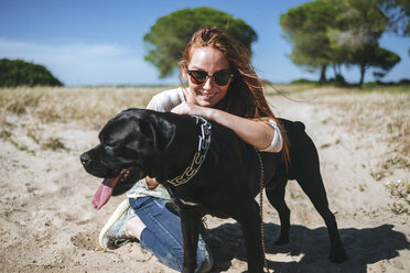 Lächelnde junge Frau mit ihrem Hund in ländlicher Landschaft - KIJF000470