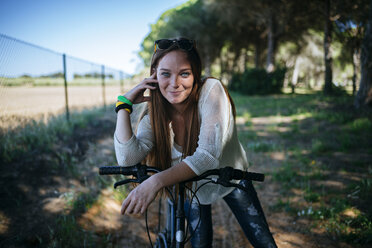 Smiling young woman with bicycle in rural landscape - KIJF000479