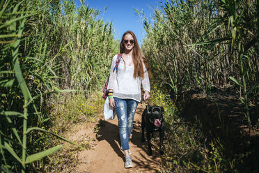 Junge Frau geht mit ihrem Hund in ländlicher Landschaft spazieren - KIJF000480
