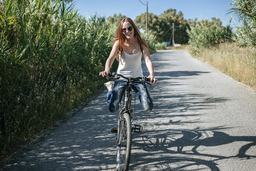 Glückliche junge Frau auf dem Fahrrad auf einem Feldweg - KIJF000482