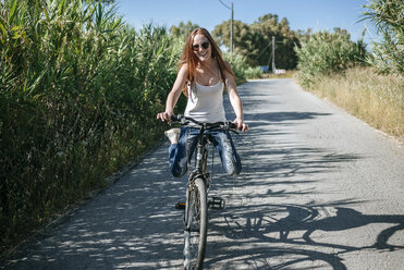 Happy young woman riding bicycle on country lane - KIJF000482