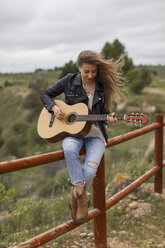 Woman sitting on wooden fence playing guitar - JPF000157