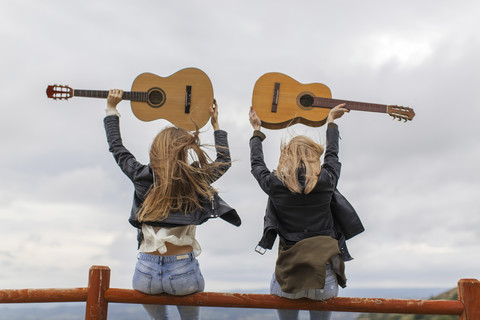 Zwei Frauen sitzen auf einem Holzzaun und heben Gitarren hoch, lizenzfreies Stockfoto