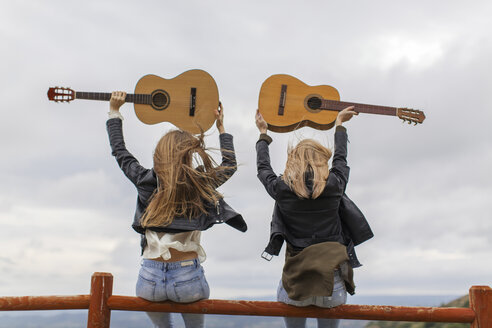 Zwei Frauen sitzen auf einem Holzzaun und heben Gitarren hoch - JPF000159