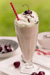 Glas Vanillemilchshake mit Vanilleeis, Sahne, Schokoladensauce und Trinkhalm, Kirschen - YFF000550