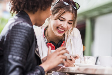 Zwei beste Freunde schauen in einem Café auf ihr Smartphone - UUF007638