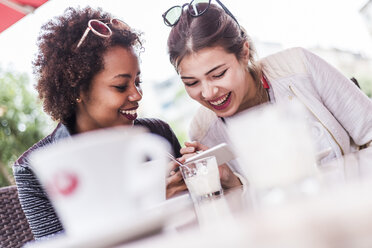 Zwei beste Freunde schauen in einem Café auf ihr Smartphone - UUF007639