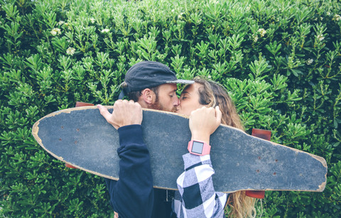 Paar küsst sich hinter Skateboard, lizenzfreies Stockfoto