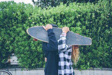 Couple hiding behind skateboard - DAPF000135