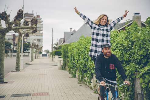 Playful couple riding bicycle on pavement - DAPF000138