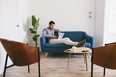 Geschäftsmann sitzt auf einer Couch im Büro und benutzt einen Laptop - EBSF001447