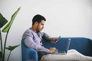 Geschäftsmann sitzt auf einer Couch im Büro und benutzt einen Laptop - EBSF001450