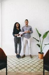 two young business people standing against wall, haolding papers and cup of coffee - EBSF001455