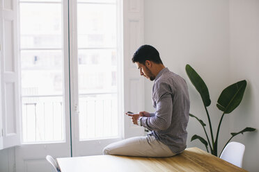 Young businessman sitting on desk using smart phone - EBSF001485