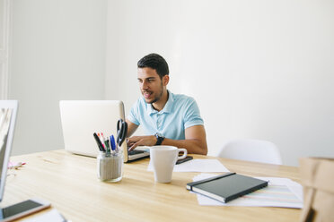 Junger Mann arbeitet im Büro und benutzt einen Laptop - EBSF001492